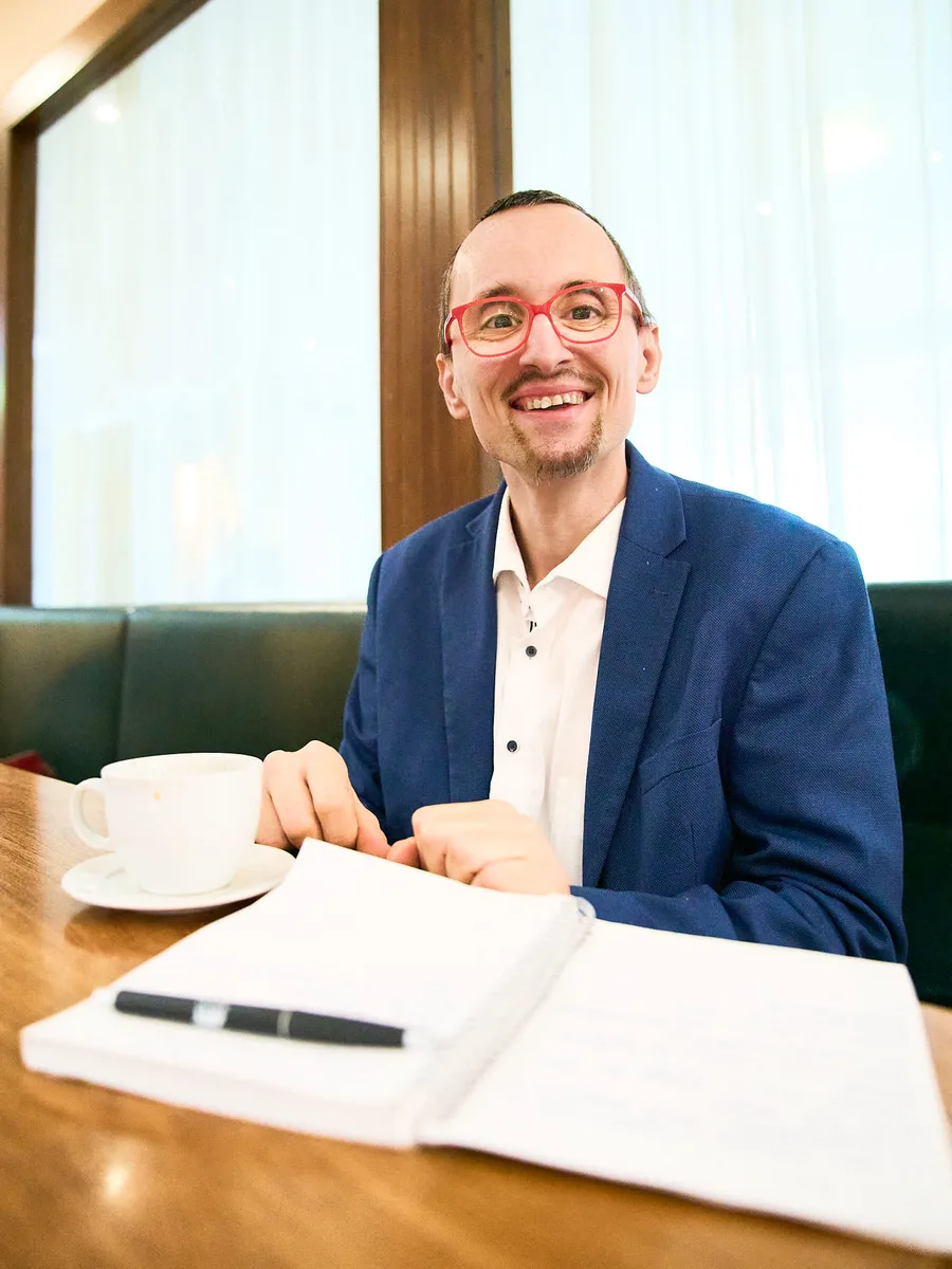 Erwin Strobl mit roter Brille und blauem Sakko an einem Tisch mit Kaffee und Notizbuch